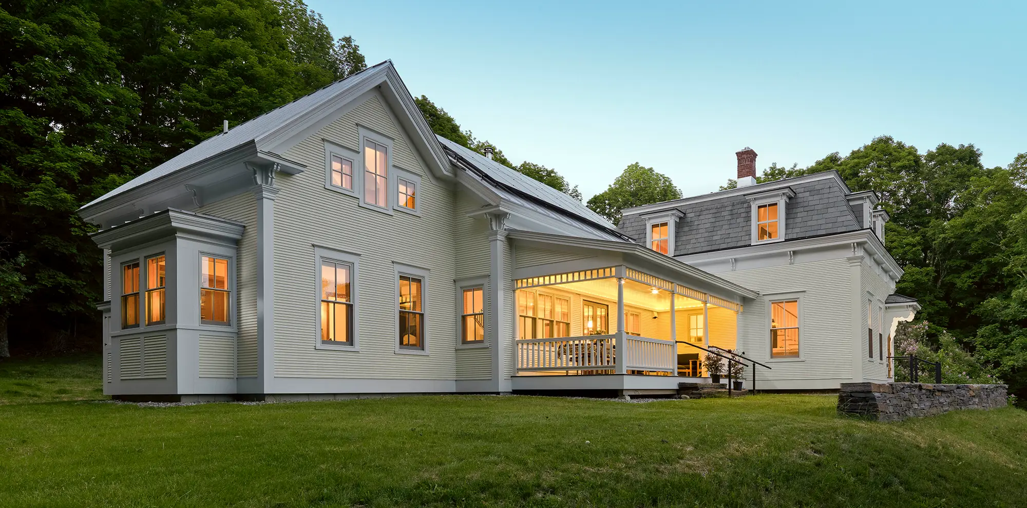 white historical multi-family home with warm lights and green trees